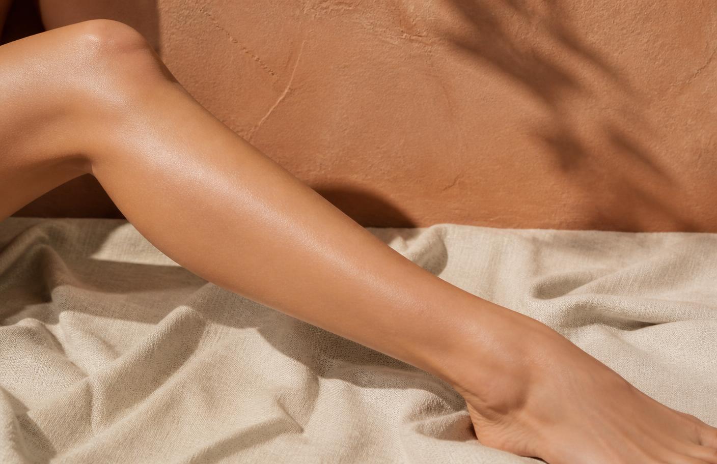 A hand guiding a white electric epilator along a smooth shin on a cream towel