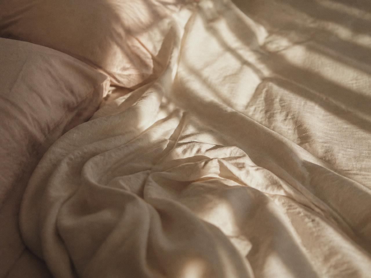 A relaxed hand resting on soft cream linen bedding in window light